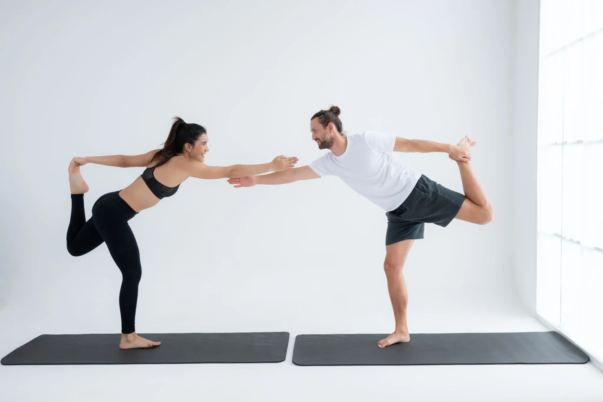 A man and woman reaching out to grab each other's arms for a 2 person dancer yoga pose.